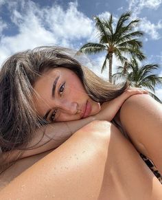 a beautiful young woman laying on top of a beach next to a palm tree and blue sky