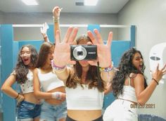 a group of women standing in front of a mirror holding up their hands to take a selfie