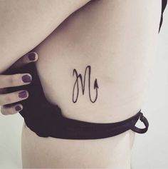 a woman's lower back tattoo with the letter m on her left ribcage