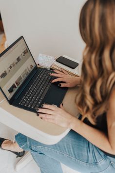 a woman sitting at a table with a laptop on her lap and looking at the screen