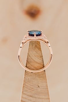 an engagement ring with a blue topazte surrounded by diamonds on a piece of wood