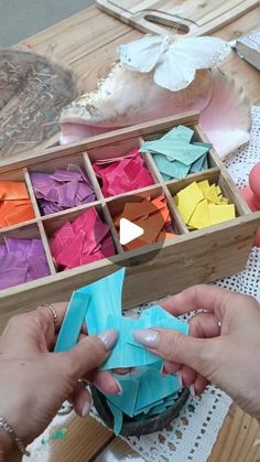 two hands are holding origami pieces in a wooden box on a doily