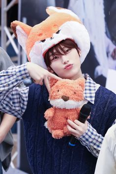 a person holding a stuffed animal in front of their face and wearing a hat with a fox on it