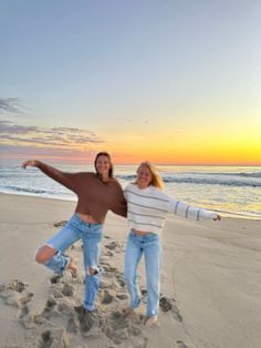 two women are posing on the beach at sunset