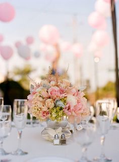 a table set up with wine glasses, plates and vases filled with pink flowers