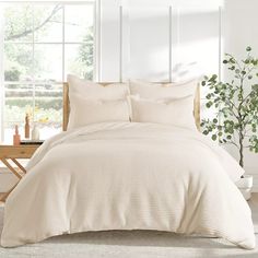 a bed with white sheets and pillows next to a plant in front of a window