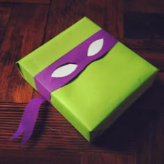 a green box with a purple mask on it sitting on top of a wooden floor