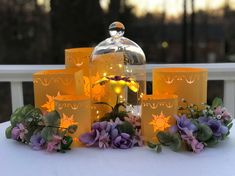 a table topped with lots of candles and flowers next to a glass jar filled with water