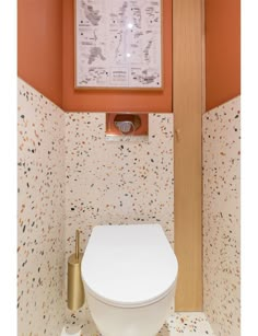 a white toilet sitting inside of a bathroom next to a wooden framed wall hanging above it