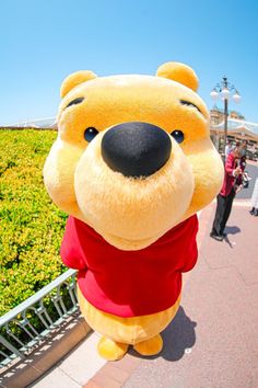 a large winnie the pooh mascot standing in front of some people on a walkway