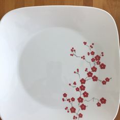 a white plate with red flowers painted on the front and side, sitting on a wooden table