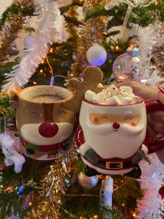 someone holding two mugs in front of a christmas tree