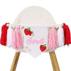 a white chair with pink tassels and strawberries on the back that says one