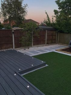 a backyard with grass and wooden decking area at dusk, lit up by lights