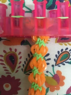 an orange and green hair comb on top of a flowered fabric with pink handles