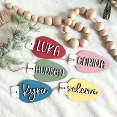 four wooden name tags are on a white sheet next to some pine cones and wood beads