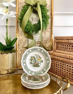 a stack of plates sitting on top of a table next to a vase filled with flowers