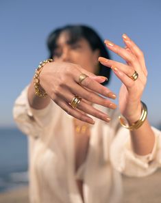 a woman holding her hands out in front of her face with two gold rings on each hand