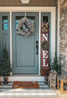 a blue front door with two christmas trees on the side and a welcome mat in front