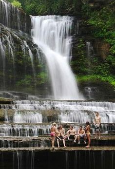 several people are sitting at the edge of a waterfall and there is water cascading over them