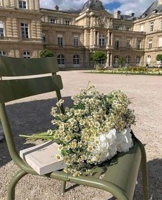 a green chair sitting in front of a building with flowers on it's back