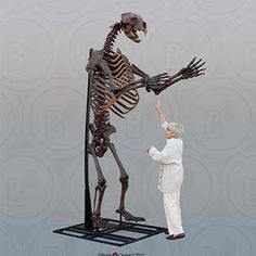 a woman standing next to a skeleton on top of a metal stand with it's arm extended