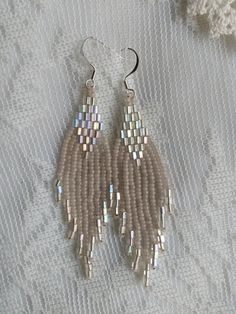 the beaded earrings are hanging from silver hooks on a white fabric surface with a small piece of yarn in the background