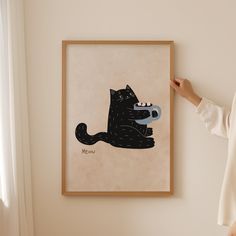 a woman standing next to a black cat on a white wall in front of a painting