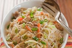 a white bowl filled with noodles and meat on top of a striped table cloth next to a fork