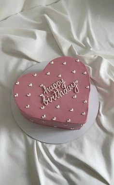 a pink heart shaped cake sitting on top of a white tablecloth covered bedding