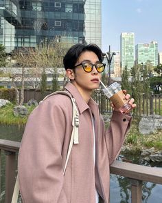 a young man wearing glasses and holding a coffee cup in his hand while standing on a bridge