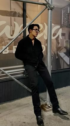 a man sitting on a metal pole in front of a store window with his legs crossed