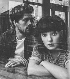 a man and woman sitting next to each other in front of a glass window with their arms crossed