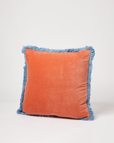 an orange and blue pillow with fringe trim on the bottom, against a white background