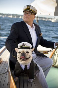 a man in a suit and tie sitting on a boat with a dog wearing a sailor's hat