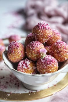 powdered sugar coated donuts in a white bowl on a gold plate with pink sprinkles