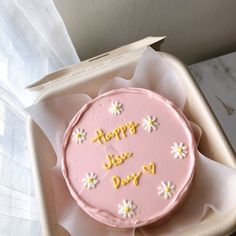 a pink cake with white flowers on it in a cardboard box that says happy birthday