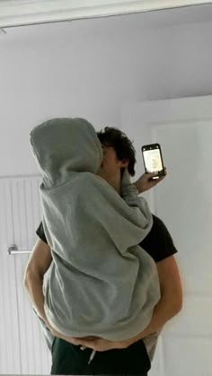 a man in a hoodie taking a selfie with his cell phone while wearing a towel