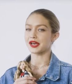 a woman holding a barbie doll in her right hand and wearing a denim shirt on the left