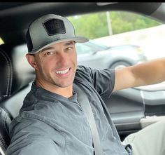 a man sitting in the driver's seat of a car wearing a baseball cap