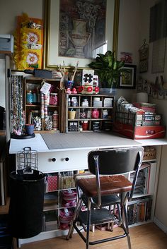 a desk and chair in a room with lots of clutter on the shelves above it