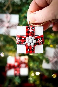 a hand holding a christmas ornament in front of a christmas tree with presents on it