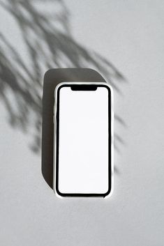 a white cell phone sitting on top of a table next to a shadow of a plant