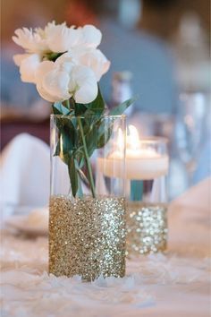 two vases filled with white flowers on top of a table covered in gold glitter