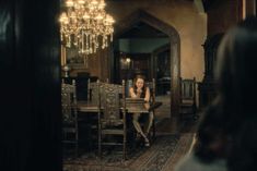 a woman sitting at a dining room table in front of a chandelier and mirror