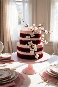 a three layer red velvet cake with white flowers on top and pink plates around it