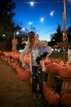 a woman holding a baby standing in front of pumpkins