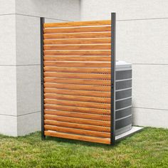 an air conditioner sitting in the grass next to a wall with wooden slats on it