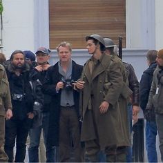 a group of men standing next to each other in front of a building with people walking around