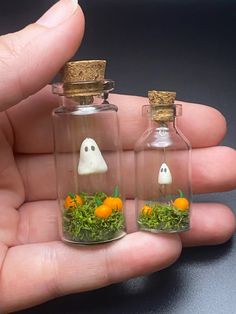 two miniature bottles with fake grass inside and ghost heads in the top one is filled with moss